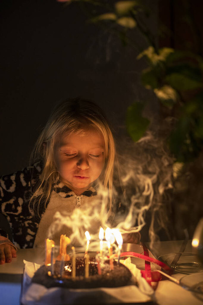 kislány elfújja gyertyák csukott szemmel születésnapi party zárlat pizsamában, homályos arc, függőleges - Fotó, kép