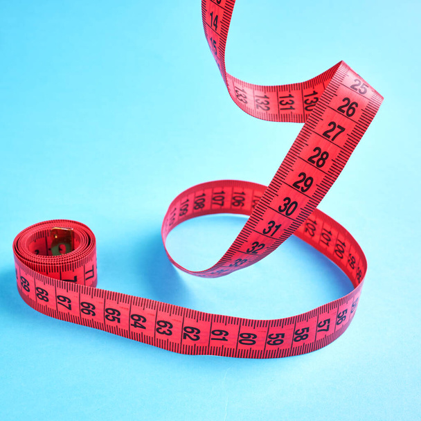 έννοια μέτρησης απώλειας βάρους. κόκκινο εκατοστό εξισορρόπηση πάνω από μπλε φόντο - Φωτογραφία, εικόνα
