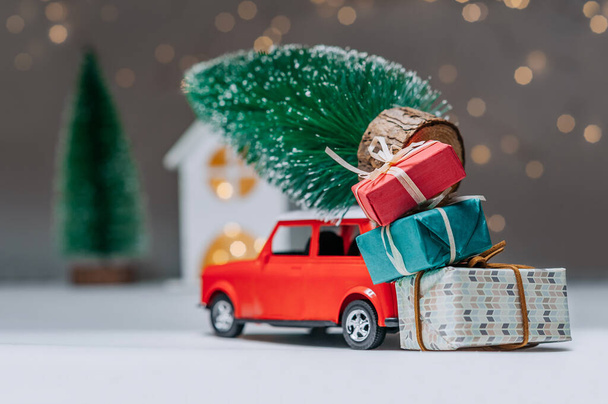 Red car with a Christmas tree on the roof. Against the background of the house. Concept on the theme of Christmas and New Year - Фото, изображение