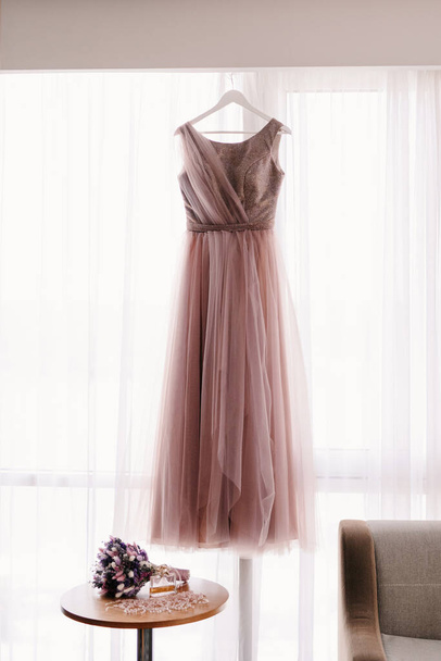 pink wedding dress on the background of the window with the bride's bouquet of dried flowers - Photo, Image
