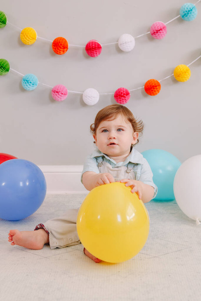 Funny Caucasian baby boy celebrating his first birthday. Child kid toddler sitting on floor with colorful balloons. Celebration of event or party indoors at home. Happy birthday lifestyle concept. - Foto, Imagem