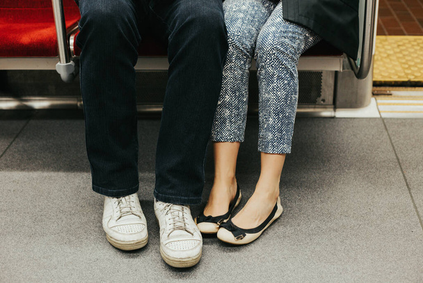 Zbliżenie nóg mężczyzny i kobiety w butach na świeżym powietrzu razem. Kilka randek siedzących razem na siedzeniach w metrze pod ziemią. Miłość i romans. Romantyczne randki. Szczegóły i części ciała. - Zdjęcie, obraz