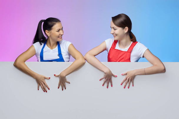 two girls in aprons pose with a white Billboard. advertising concept - Фото, зображення