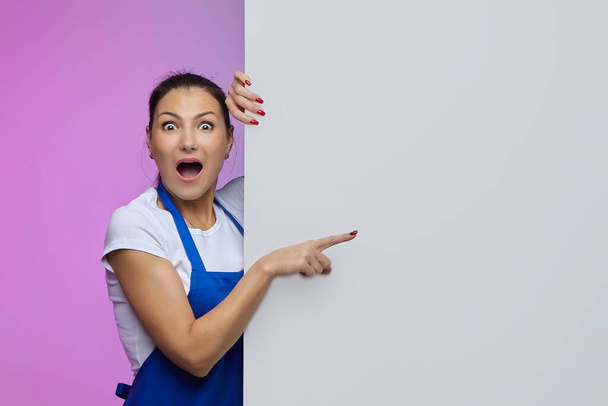 working girl in a blue apron of Asian appearance poses with a white Billboard. advertising concept - Фото, изображение
