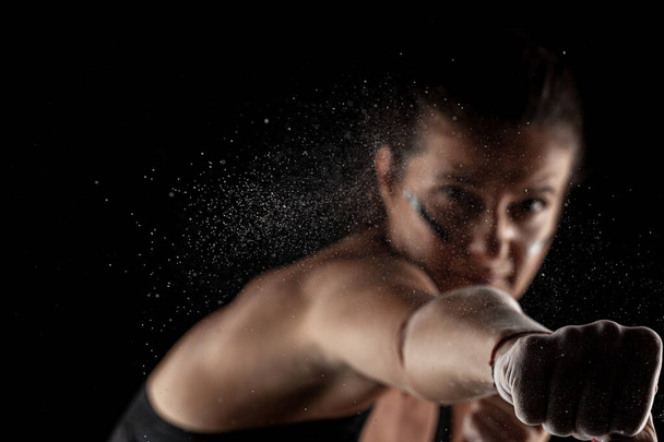 Kickboxer kirl with magnesium powder on her hands, punching with dust visible. - Foto, Bild
