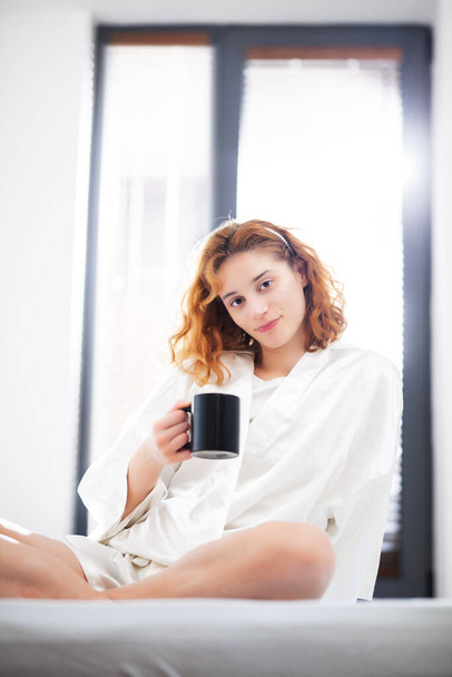 Happy careless girl at home. Lying in bed drinking coffee or tea in the morning. - Foto, Imagem