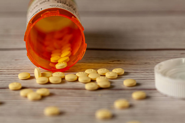 Un frasco de medicamentos de prescripción naranja se volcó sobre una mesa de madera con pastillas redondas de color amarillo esparcidas por la superficie. Una imagen versátil para la salud, enfermedad, recuperación, abuso, dependencia, sobredosis - Foto, Imagen
