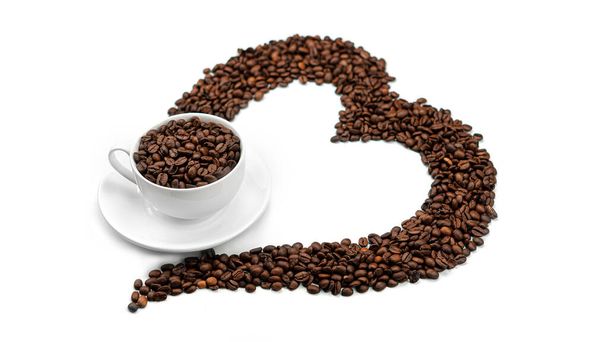 Una taza con granos de café y un corazón hecho de granos de café sobre un fondo blanco. Foto de alta calidad - Foto, imagen