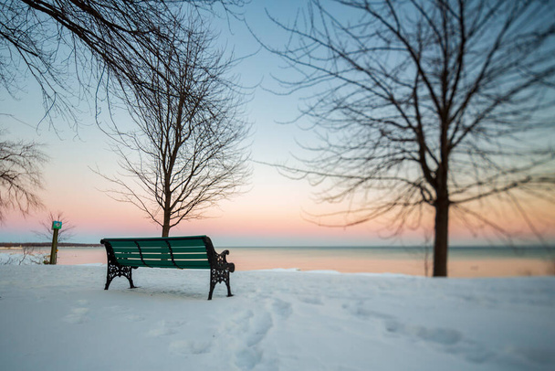 Скамейка в зеленом парке сидит на снежном поле и, используя объектив Tilt-shift, захватывается лицом к озеру Онтарио.. - Фото, изображение