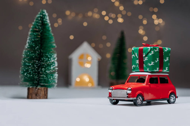 A red car on the background of a forest and a house will bring Christmas New Year gifts - Fotoğraf, Görsel