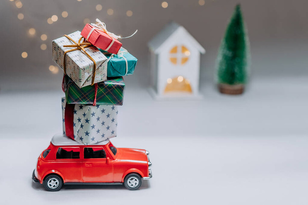 A red car on the background of a forest and a house will bring Christmas New Year gifts - Фото, изображение
