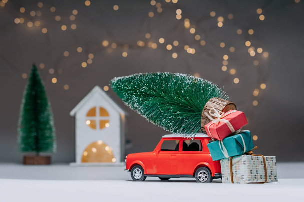 Red car with a Christmas tree on the roof. Against the background of the house. Concept on the theme of Christmas and New Year - Foto, afbeelding