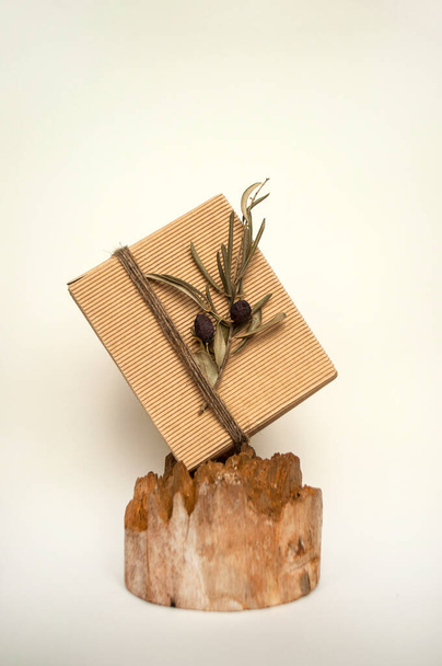 Geschenkbox in Bastelpapier gewickelt, mit Bindfäden und einem Olivenzweig auf einem schönen Holzstumpf. - Foto, Bild
