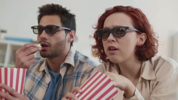 zbliżenie do kręcone kaukaskie dziewczyna i mieszane wyścig młody człowiek noszenie okulary 3D, rozmowa, jedzenie popcorn, oglądanie film w domu - Materiał filmowy, wideo