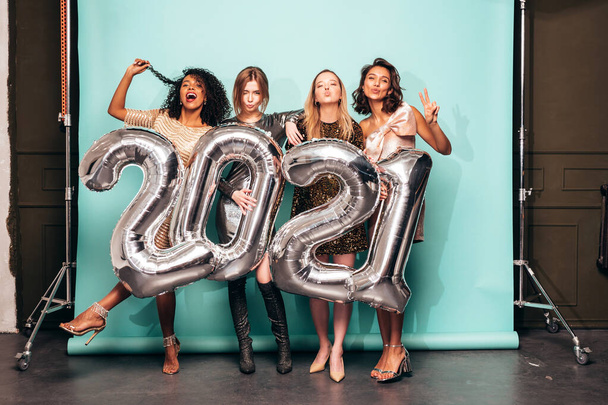 Beautiful Women Celebrating New Year.Happy Gorgeous Female In Stylish Sexy Party Dresses Holding Silver 2021 Balloons, Having Fun At New Year's Eve Party. Holiday Celebration.Charming Models  - 写真・画像
