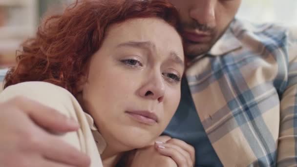 Zbliżenie młodej niebieskookiej białej kobiety z miedzianymi włosami płaczącej na piersi przyciętego partnera w szachownicy klepiącej ją po ramieniu - Materiał filmowy, wideo