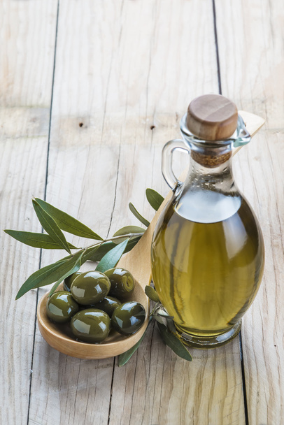 olijfolie fles en een lepel met olijven - Foto, afbeelding