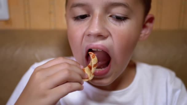 Hambriento caucásico adolescente pone patatas fritas en la boca con la mano. Chico come comida rápida. - Metraje, vídeo