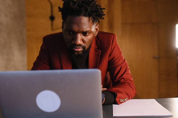 a focused black man in a suit is working on a laptop. Remote work from home - Foto, Imagen