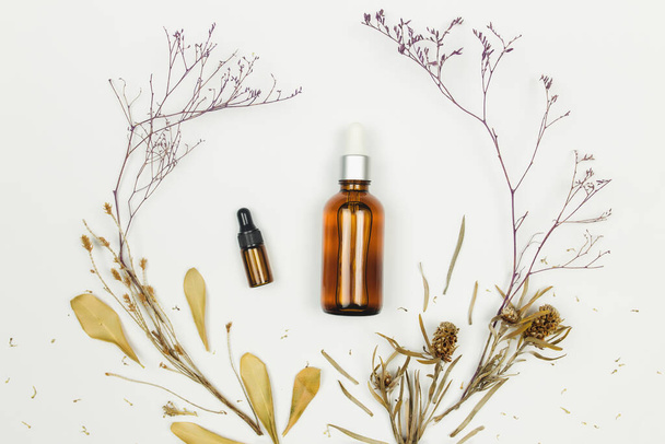 Butelki oleju kosmetycznego z suszonymi ziołami na białym tle - Zdjęcie, obraz