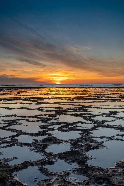 Вертикальний вид на прекрасний захід сонця над океаном з кам'янистим пляжем і припливними басейнами на передньому плані
 - Фото, зображення