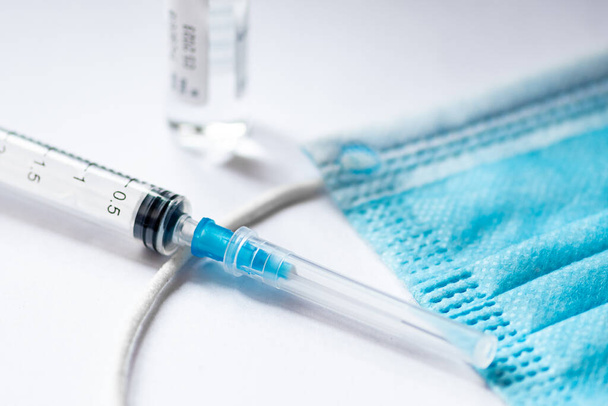 Ruisku, injektiopullo ja kirurginen kasvonaamio valkoisella pöydällä käyttövalmiina. Covid- tai Coronavirus-rokotteen tausta - Valokuva, kuva