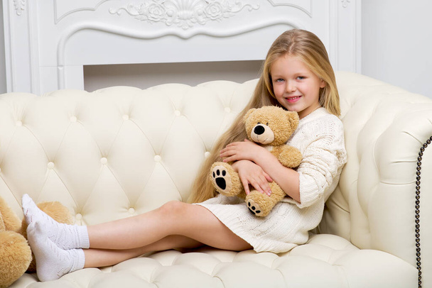 Girl sitting on sofa hugging teddy bear - Фото, изображение