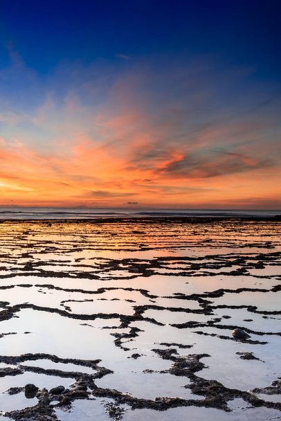 A vertical view of a beautiful sunset over the ocean with rocky beach and tidal pools in the foreground - Photo, Image