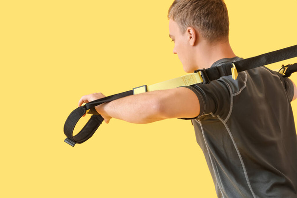 Sporty young man training with TRX straps on color background - Foto, imagen