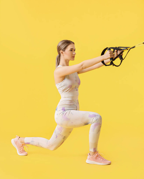 Sporty young woman training with TRX straps on color background - Фото, изображение