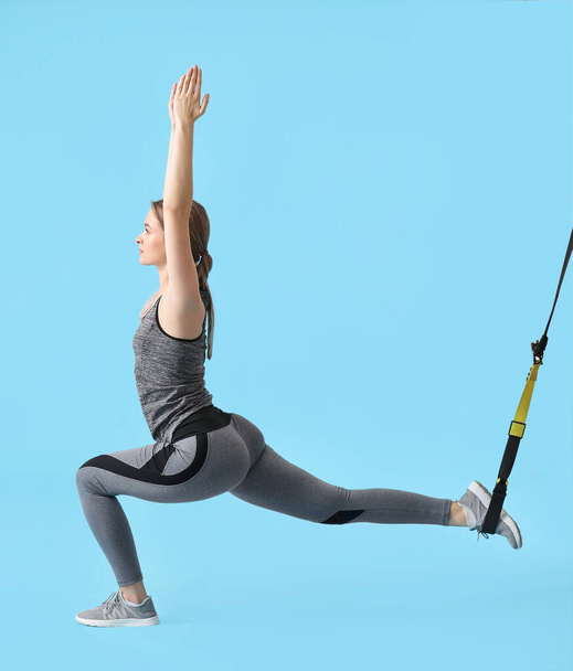Sporty young woman training with TRX straps on color background - 写真・画像