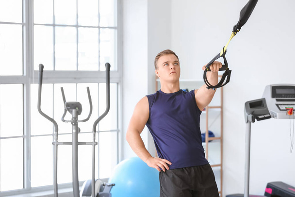 Sporty young man training with TRX straps in gym - Photo, Image