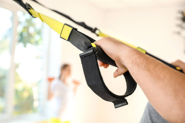 Sporty young man training with TRX straps in gym, closeup - Photo, Image