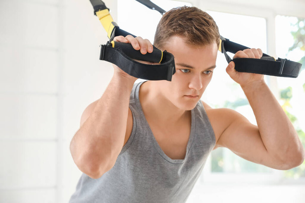 Sporty young man training with TRX straps in gym - Foto, afbeelding