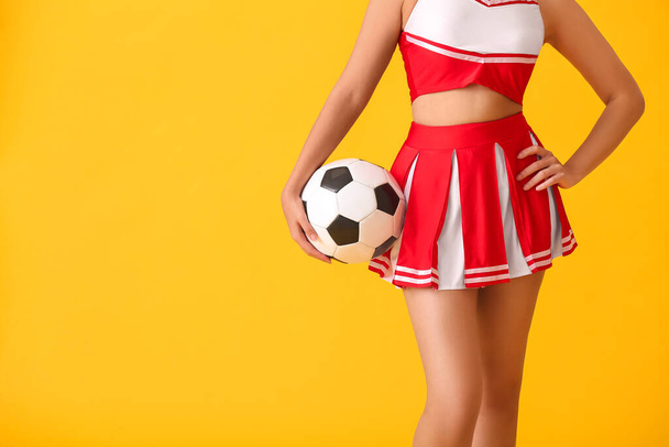 Hermosa animadora joven con pelota de fútbol sobre fondo de color - Foto, imagen