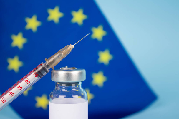 Φιαλίδιο εµβολίου COVID-19 κατά της σημαίας της ΕΕ σε κυανό φόντο µε χώρο αντιγραφής για κείµενο - δόσεις εµβολίου του κορωναϊού, ιδέα εµβολιασµού στην Ευρώπη, επιλεκτική εστίαση - Φωτογραφία, εικόνα