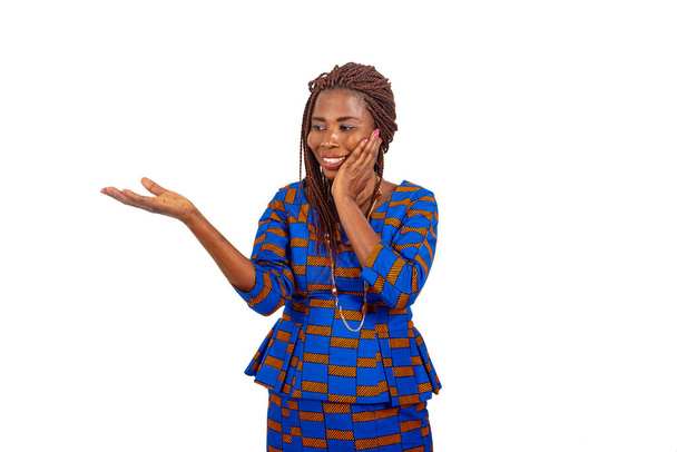 piękna afrykańska businesswoman w tradycyjnej sukience stojącej na białym tle patrząc na jej wyciągniętą rękę uśmiecha się z drugiej strony na policzku - Zdjęcie, obraz