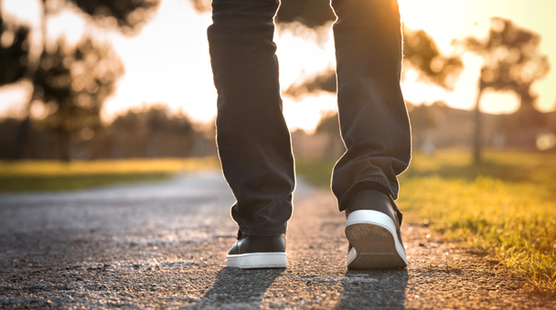 Mann, der bei Sonnenuntergang im Park spazieren geht. Nahaufnahme auf Schuhen. Konzept von Neuanfang und Freiheit - Foto, Bild