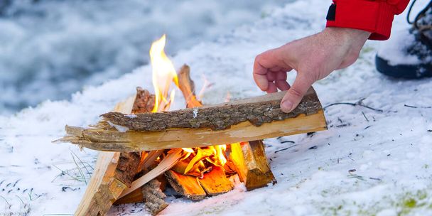 cozy fire on the river bank in winter. small warm bonfire in winter time. campfire by the river on snow an winter season - Photo, Image