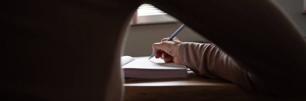 Κάτω από το χέρι μιας γυναίκας που γράφει στο σημειωματάριο στο σπίτι. - Φωτογραφία, εικόνα