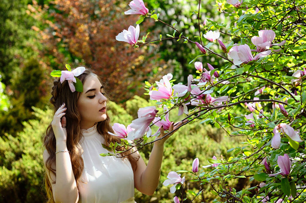 春の庭に咲くマグノリアと若い魅力的な女性の肖像画。春の背景。女の日だ。グリーティングカード.  - 写真・画像