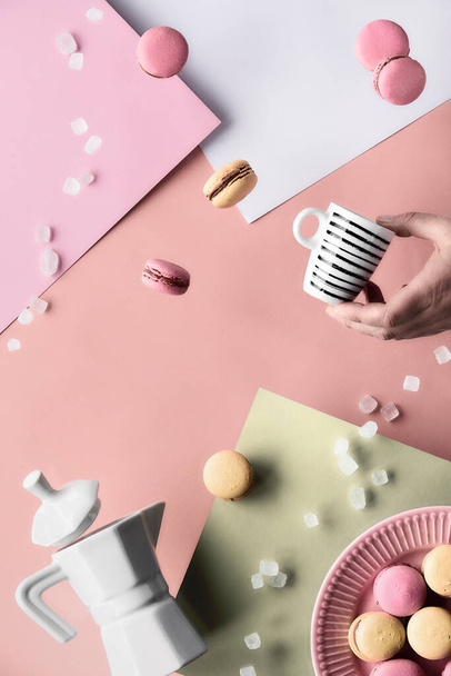 Levitation and balance composition. Flying macaroons, ceramic coffee maker and hand with espresso coffee cup. Geometric layered paper background in pastel colors, pink, cream and light green. - Фото, изображение