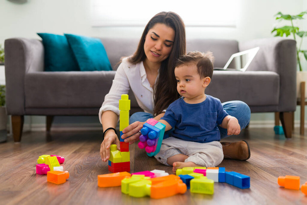 Single mom and baby sitting on living room floor playing with building block toys - 写真・画像