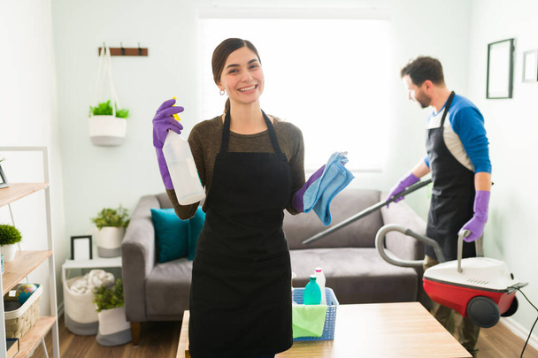 Hermosa joven con un delantal y guantes y disfrutar de la limpieza de su casa junto con su novio - Foto, Imagen