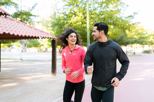 Fit latin couple smiling and enjoying a run in the park. Good-looking guy and pretty woman flirting while going on a run outdoors - Photo, Image