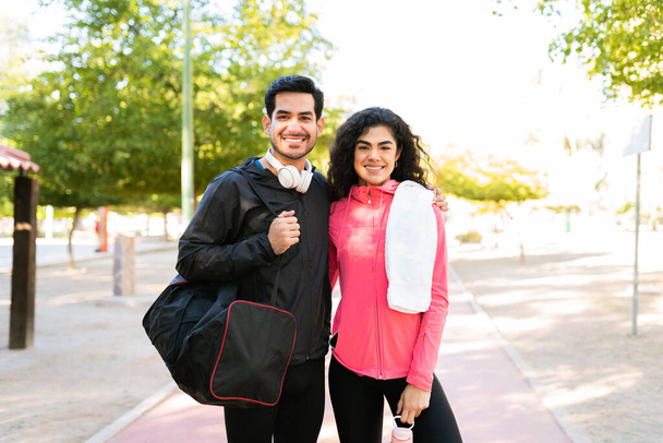 Mutlu ve atletik genç çift parkta bir spor çantası, havlu ve su şişesi taşıyorlar. - Fotoğraf, Görsel