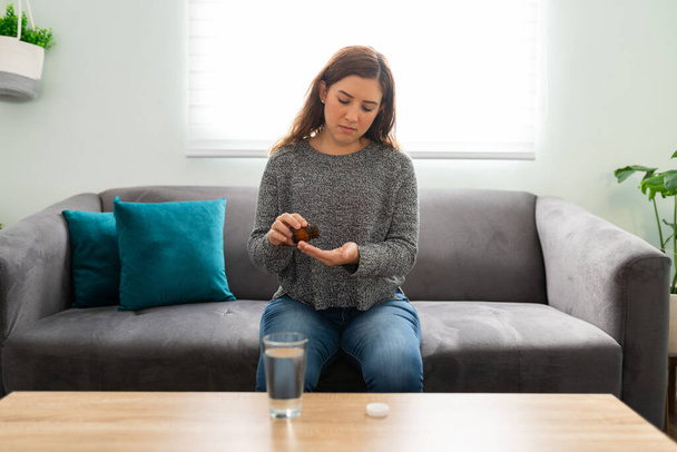 Kaunis sairas nuori nainen istuu sohvalla ja aikoo ottaa hänen huumeiden pillereitä lasillisella vettä - Valokuva, kuva