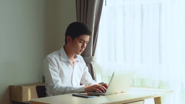 Jonge Aziatische man zit aan de tafel werken op laptop, mooie Aziatische vrouw brengt hem kopje koffie te ondersteunen en aan te moedigen en te helpen om te ontspannen tijdens het werk van thuis uit. - Video