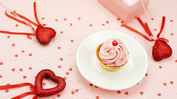 Вкусный торт с розовым кремом среди красных сердец на палочке на розовом фоне. День Святого Валентина. - Фото, изображение