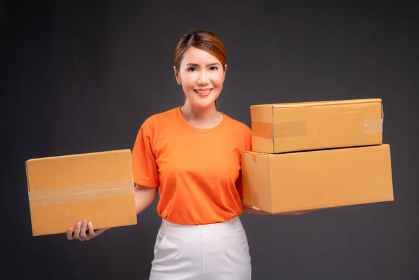 Livraison femme asiatique ou messager portant un uniforme orange tient une boîte en carton en studio. - Photo, image